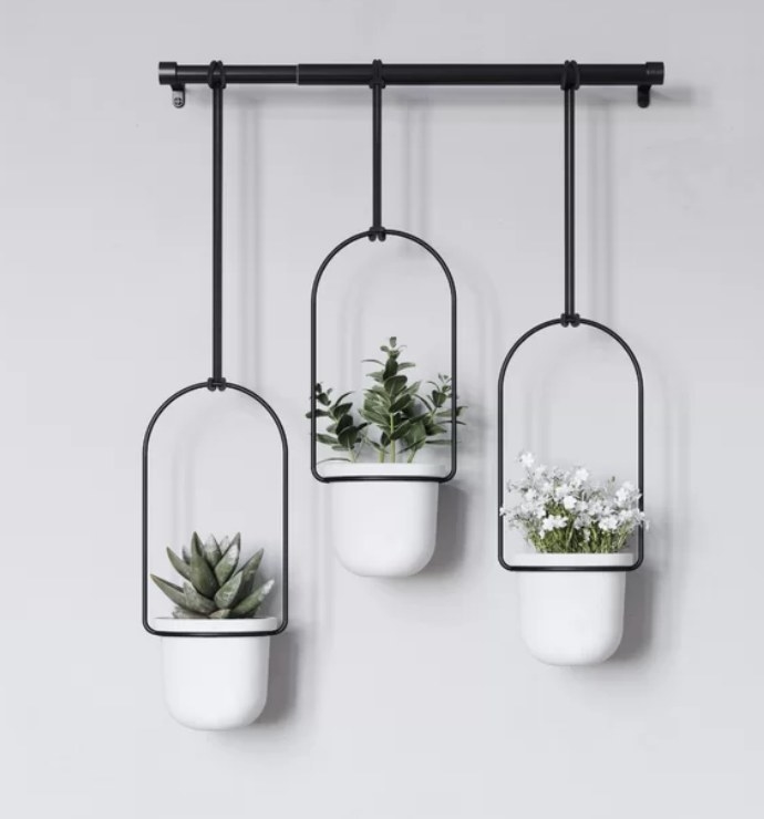 Black rod with three black hanging ropes holding white planters with plants