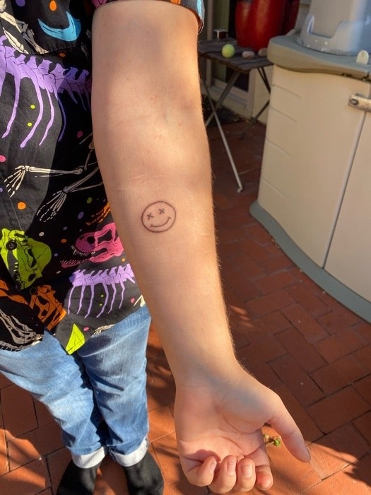 A smiley face tattoo with X&#x27;s for eyes on someone&#x27;s forearm