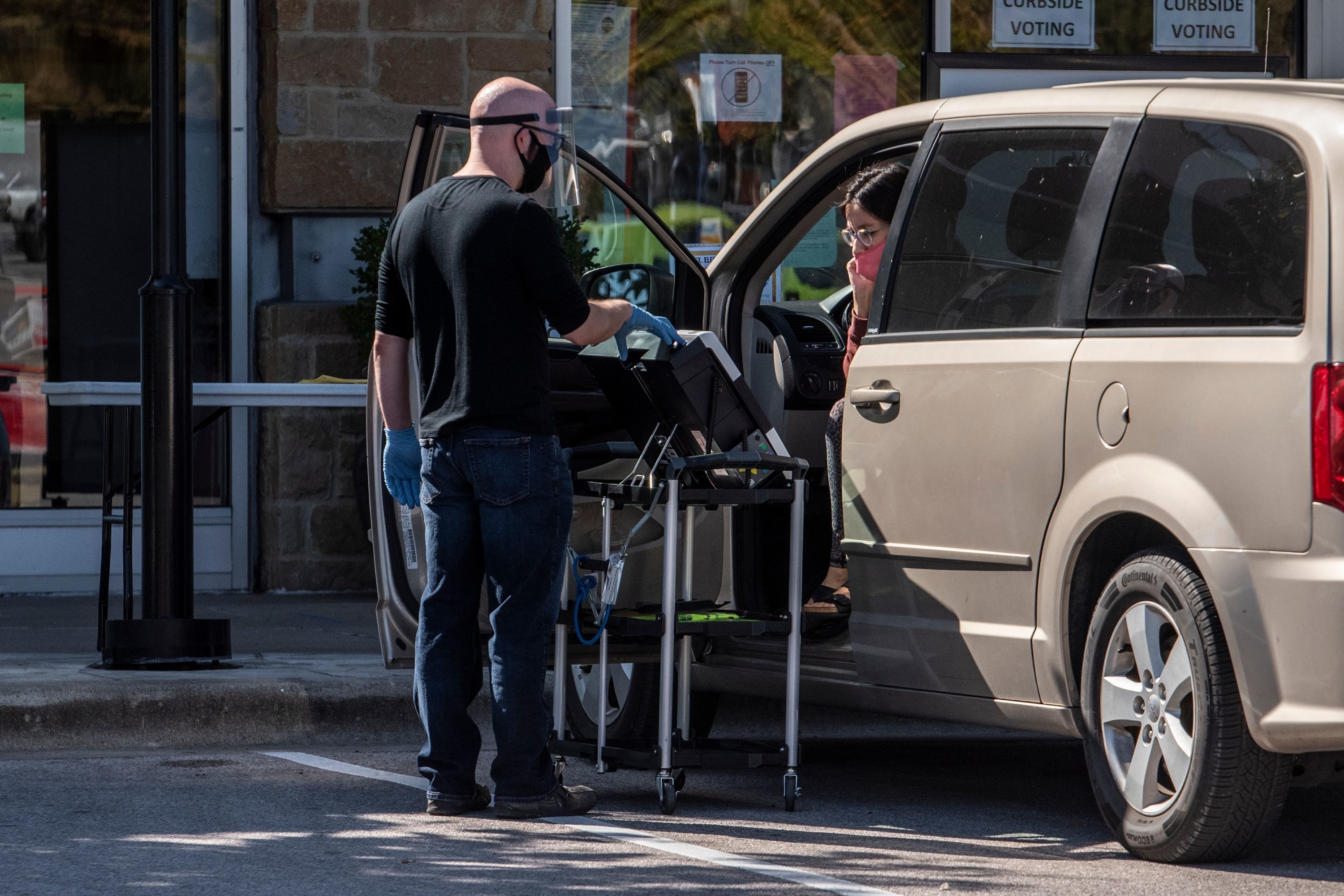 Man holding a ballot at a station outsdie a woman&#x27;s car. 