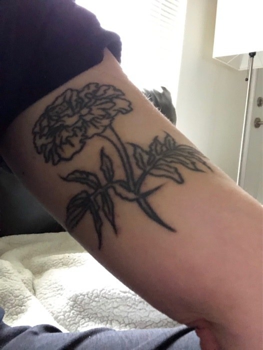A large black outline of a flower with its stem and leaves on someone&#x27;s arm