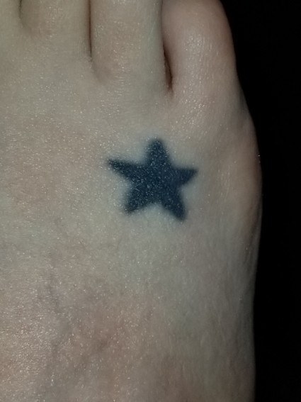 A small, solid star tattoo on someone&#x27;s right foot