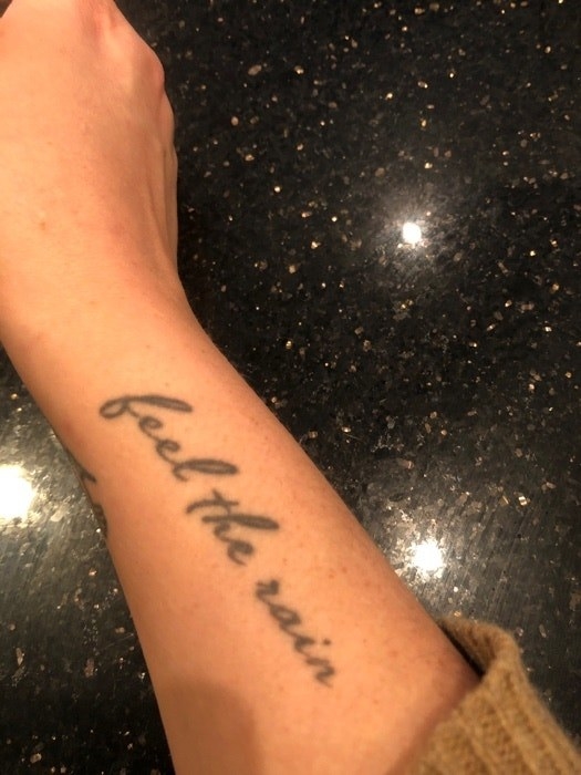 A tattoo that says, &quot;feel the rain,&quot; in black cursive on the inner side of someone&#x27;s forearm