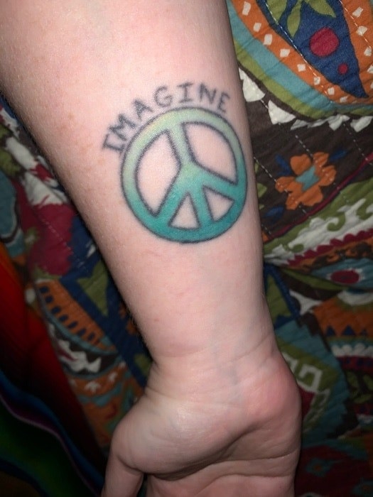 A peace sign colored in with a faded green gradient and the word &quot;imagine&quot; above it on someone&#x27;s forearm 