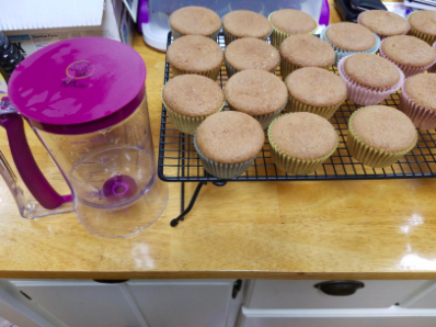 the batter dispenser with cupcakes cooling on a kitchen counter