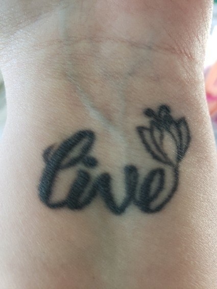 A tattoo that reads, &quot;live,&quot; as the end of the &#x27;E&#x27; curves up into a blossoming flower on the inside of someone&#x27;s wrist