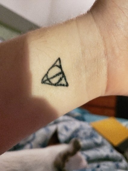 A tattoo of the Deathly Hallows symbol from Harry Potter on someone&#x27;s wrist in black ink