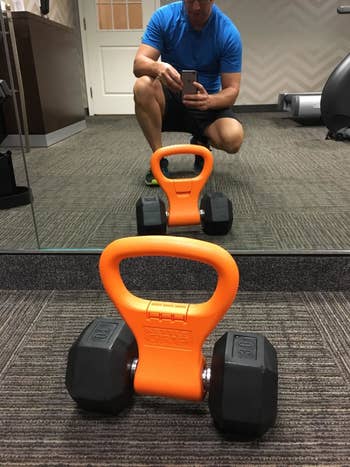 Reviewer pic of the orange Kettle Gryp around a black dumbbell on the floor