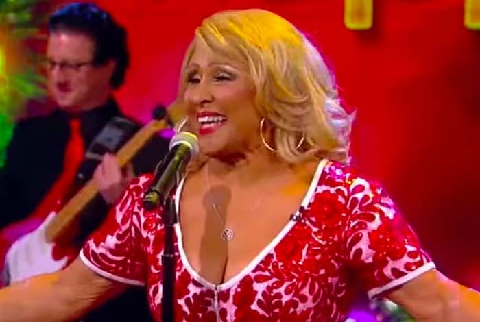 Darlene Love sings in front of a microphone wearing a red and white patterned top