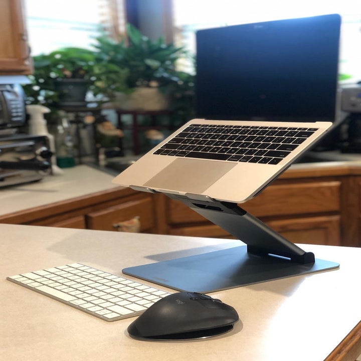 A reviewer photo of the laptop stand partially extended sitting on a countertop next to a wireless keyboard and mouse 