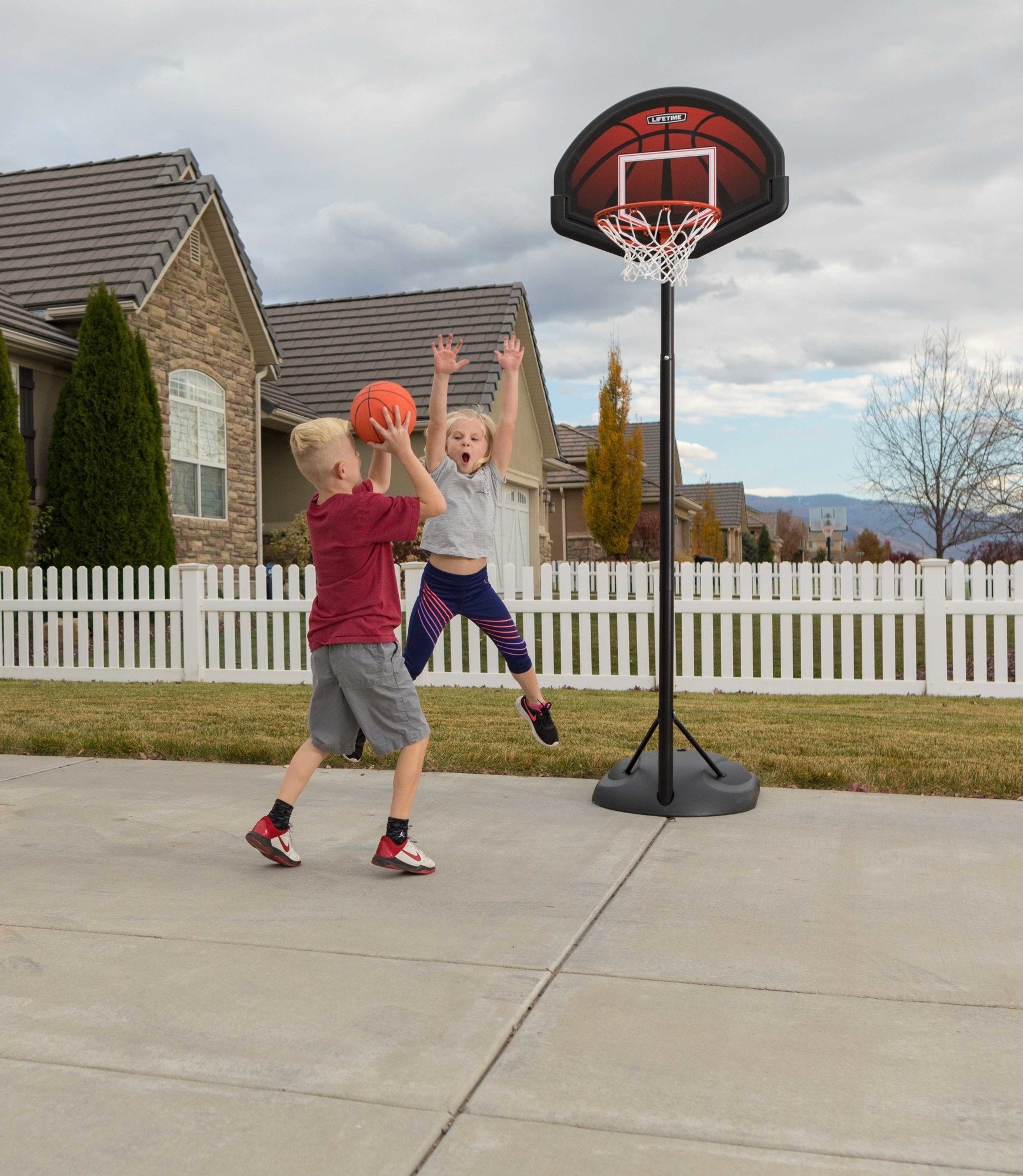two kids playing basketball in their front driveway