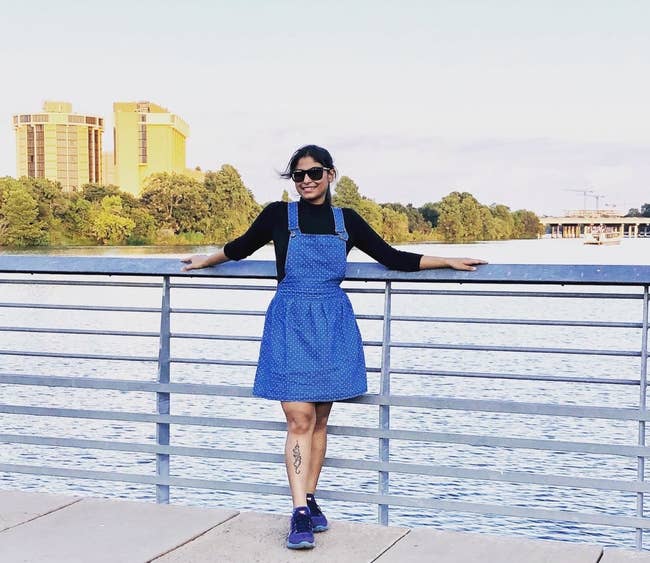A reviewer wearing the above-the-knee, flared, polka dot, blue denim pinafore 