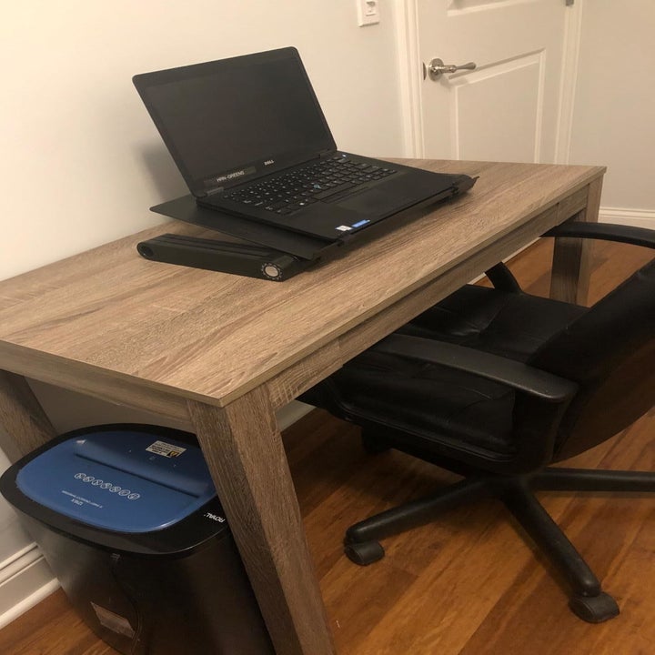 Reviewer photo of the laptop stand sitting on a desk, collapsed down all the way so the laptop can be used while sitting 