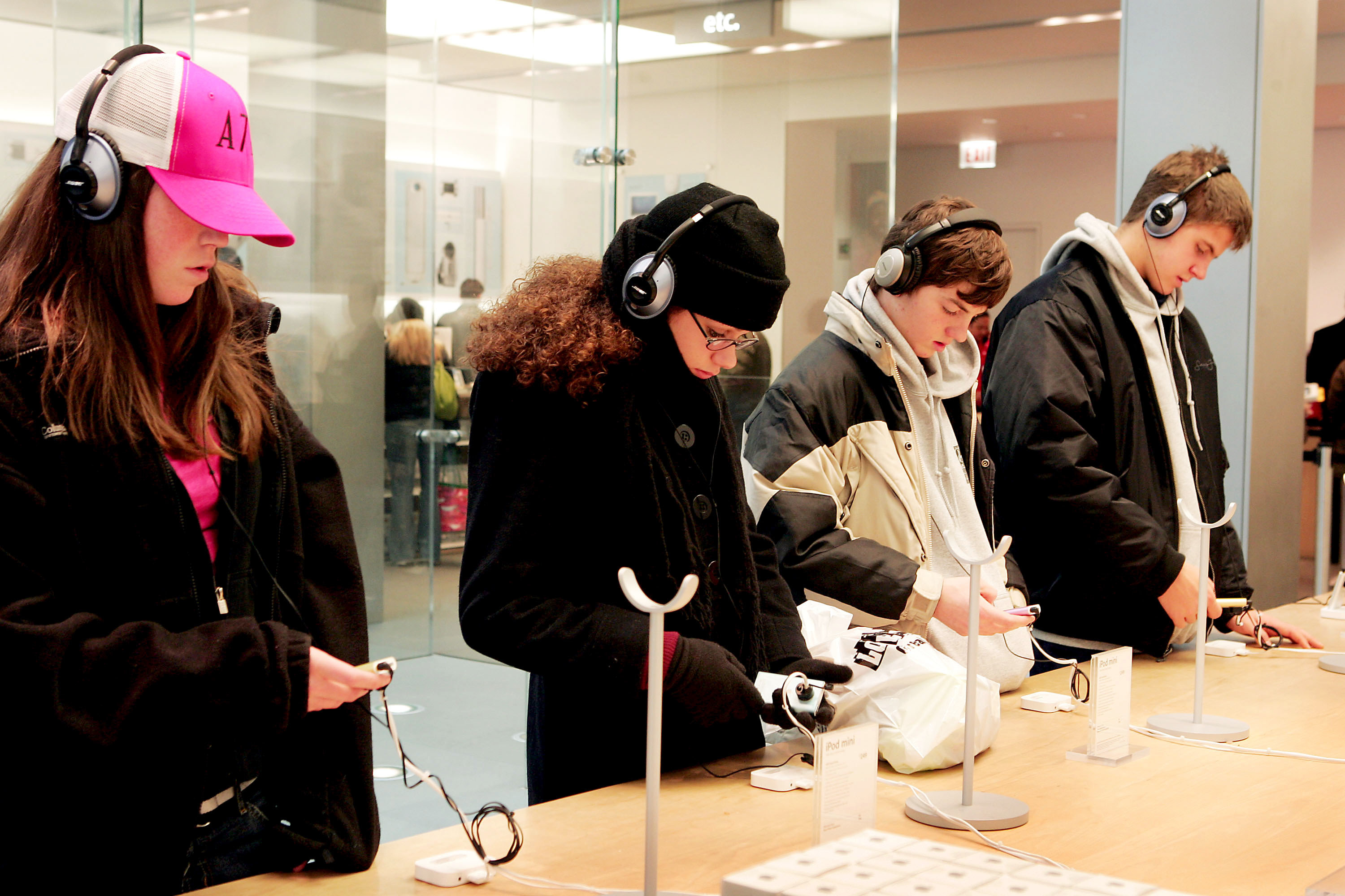 Picture of a four teens each looking at an iPod and wearing headphones inside an Apple Store 