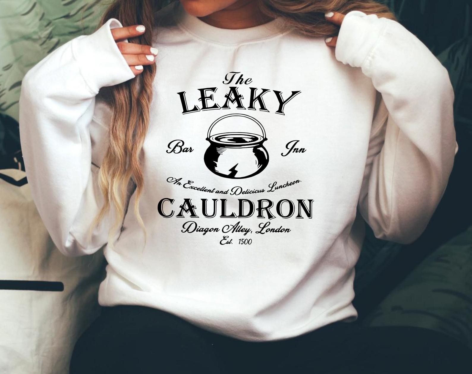 model wearing white sweatshirt that says the Leaky Cauldron in black