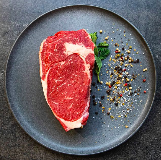 Uncooked steak on plate beside seasoning 