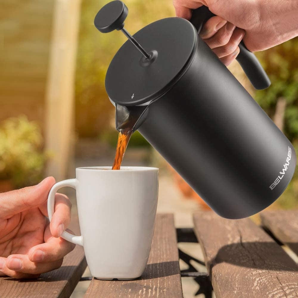 A close up of a person pouring coffee from the French press into someone&#x27;s mug
