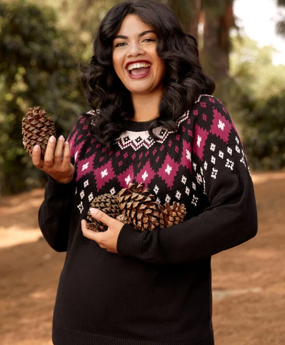 A person wearing a knit sweater and cradling a bunch of pinecones in their arm