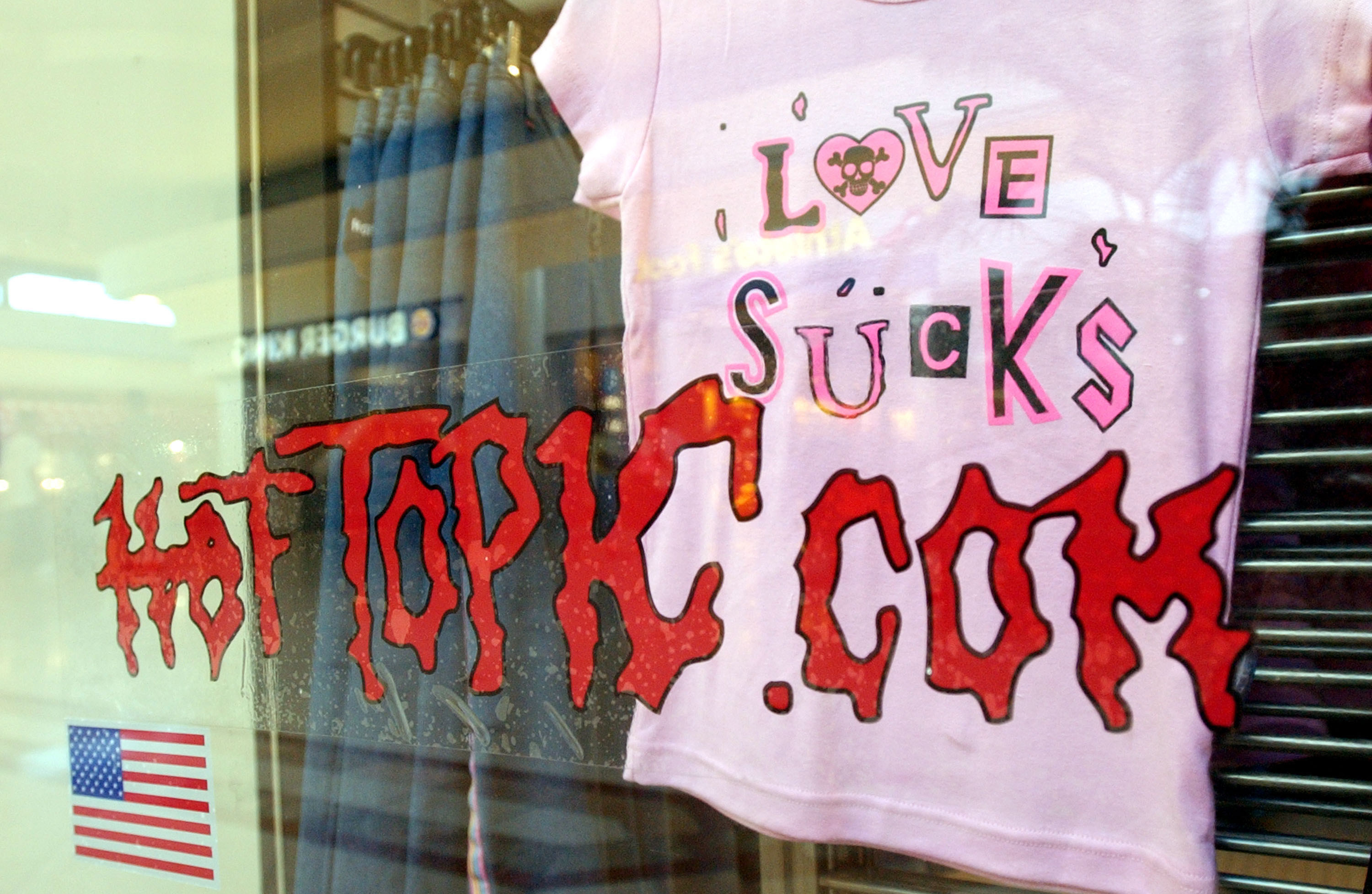 A pink Love Sucks T-shirt hanging on display in the window of a Hot Topic
