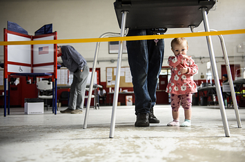 Baby stands at her father's feet at a ballot station on Election Day. 