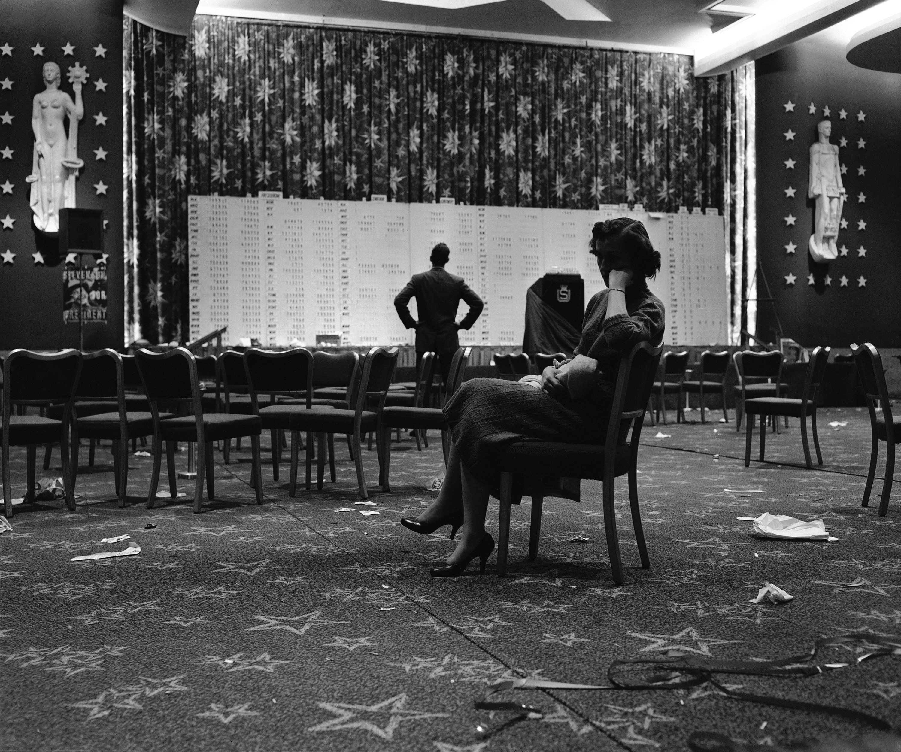 A woman in a chair looking sad in an empty hall.