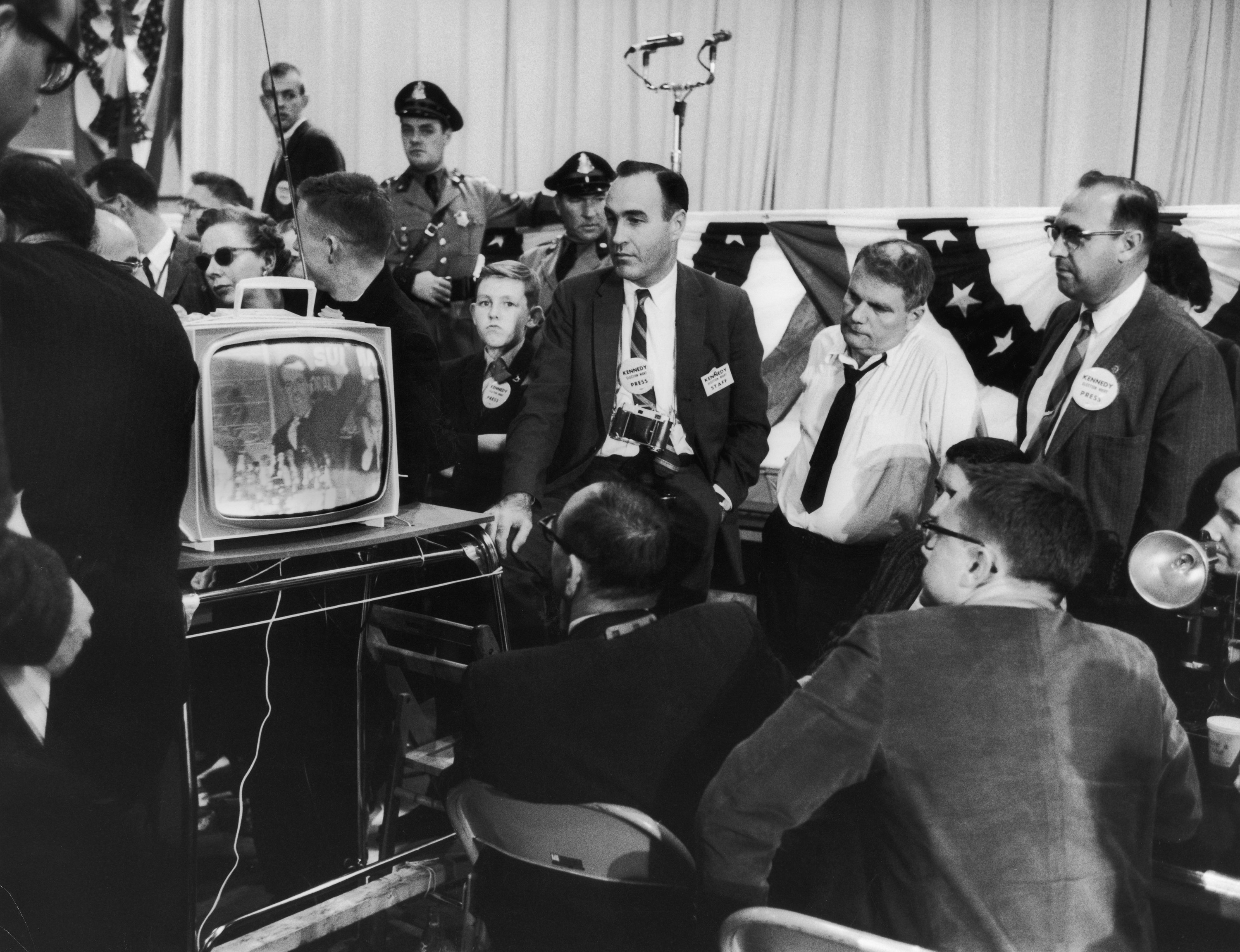 Men in black-and-white photo crowded around a TV