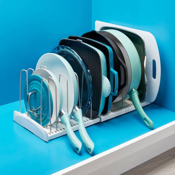 White cookware rack with gray dividers holding blue and green pans