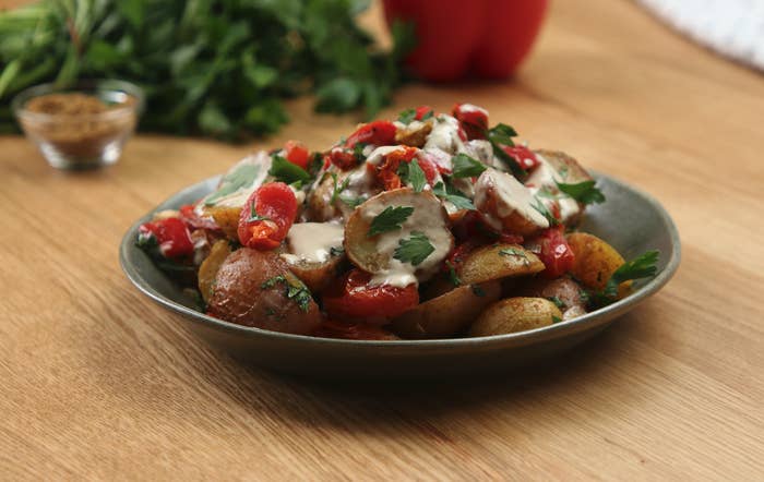 A plate of roasted little potatoes covered in red peppers, tahini and parsley.