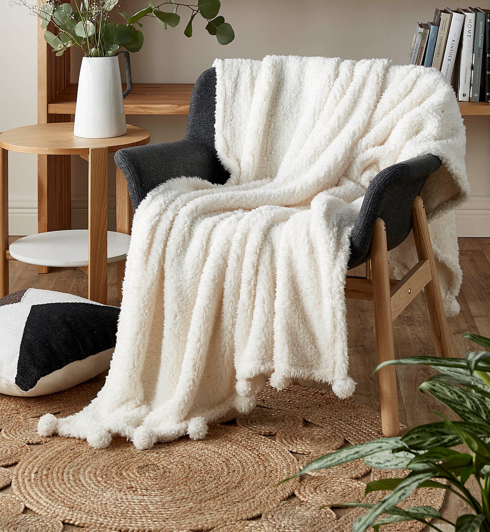 A soft sherpa blanket with pom poms on the trim draped over a chair
