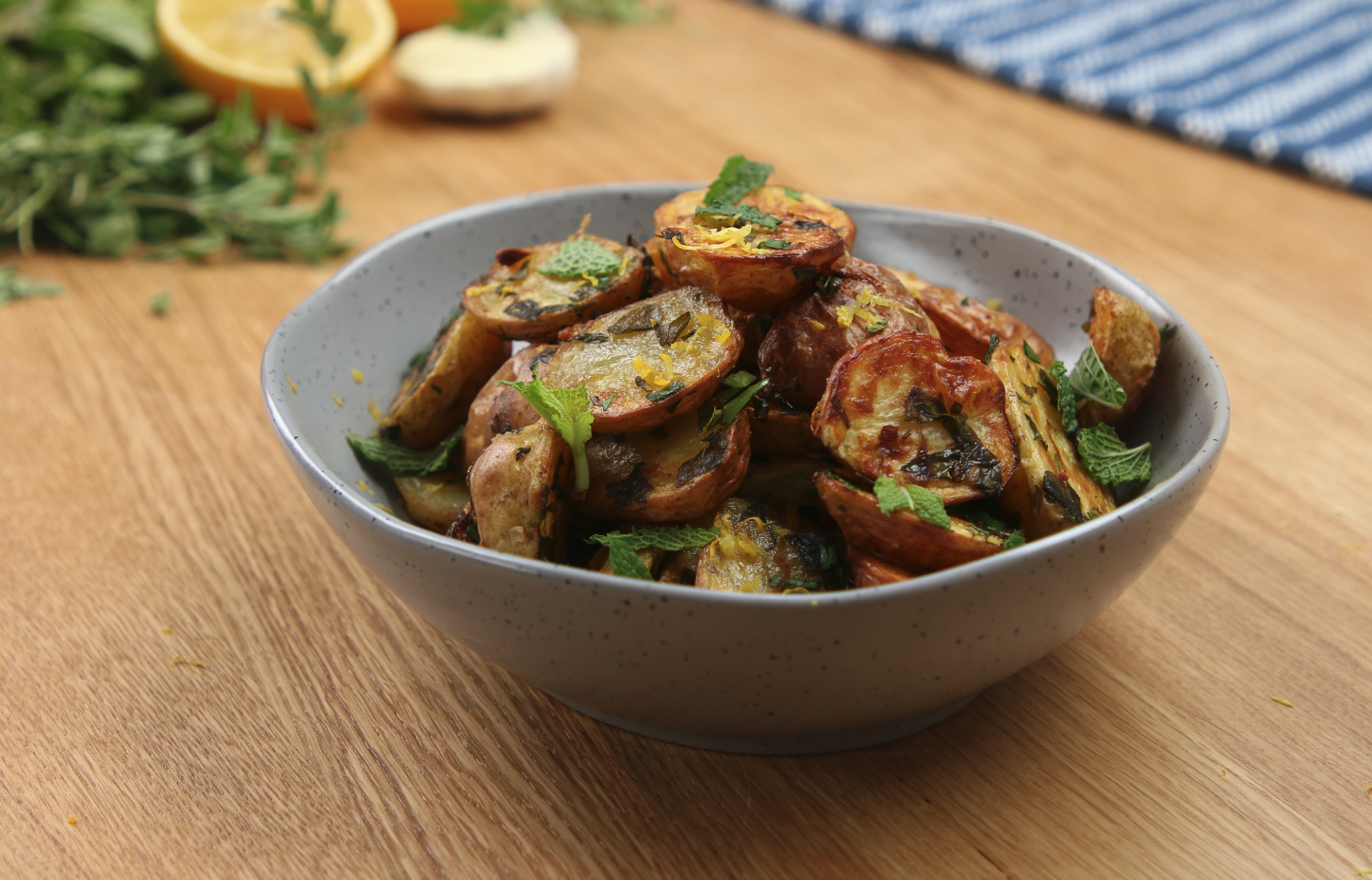 A bowl of roasted little potatoes cut in half covered in lemon zest and mint.