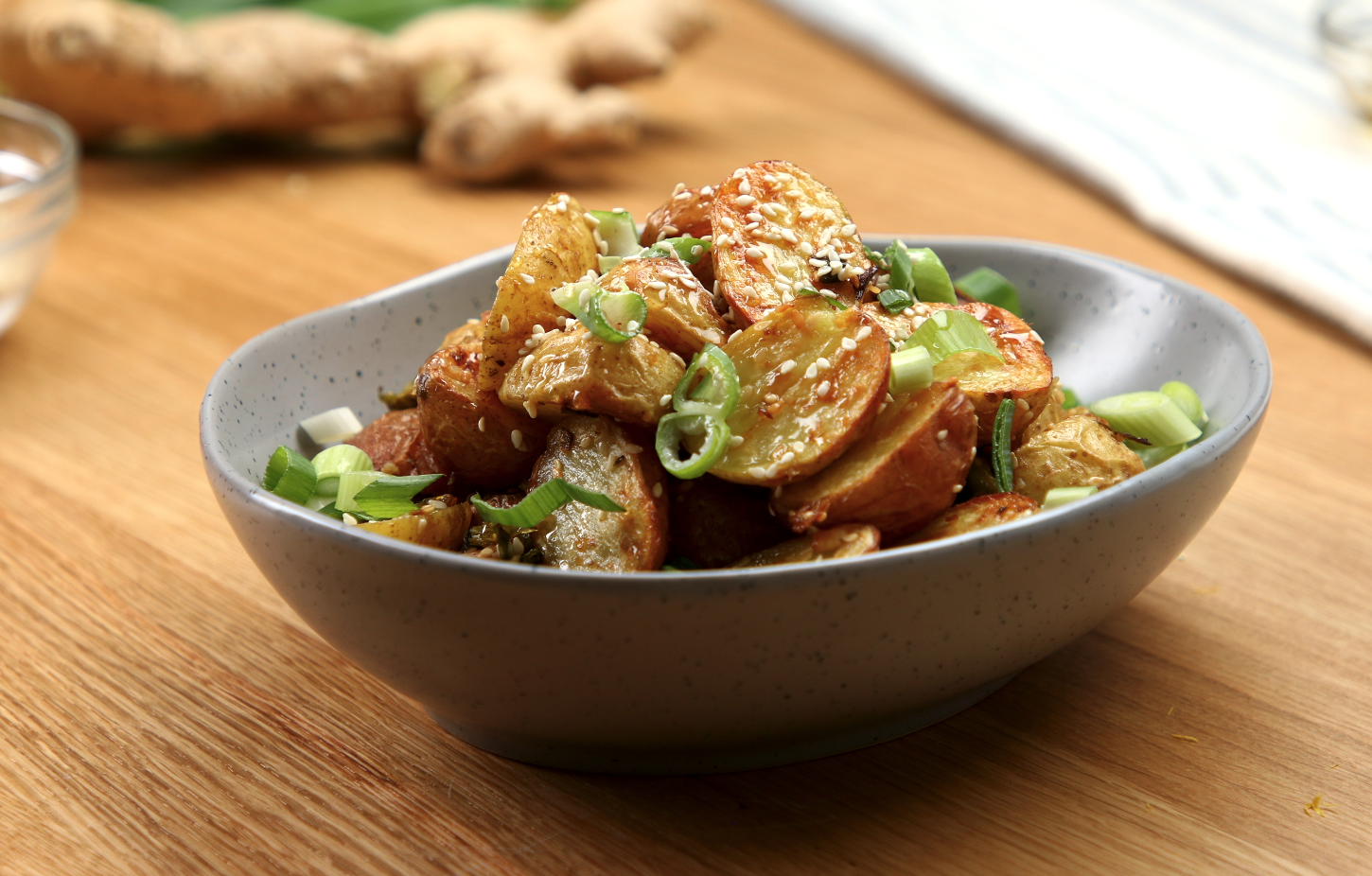 A bowl of roasted little potatoes covered in green onions, honey and sesame seeds