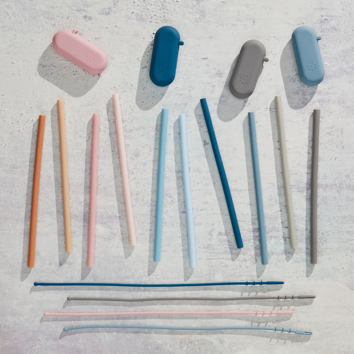 Ten reusable silicone straws, four travel cases, and four cleaning squeegees laid out on a gray surface 