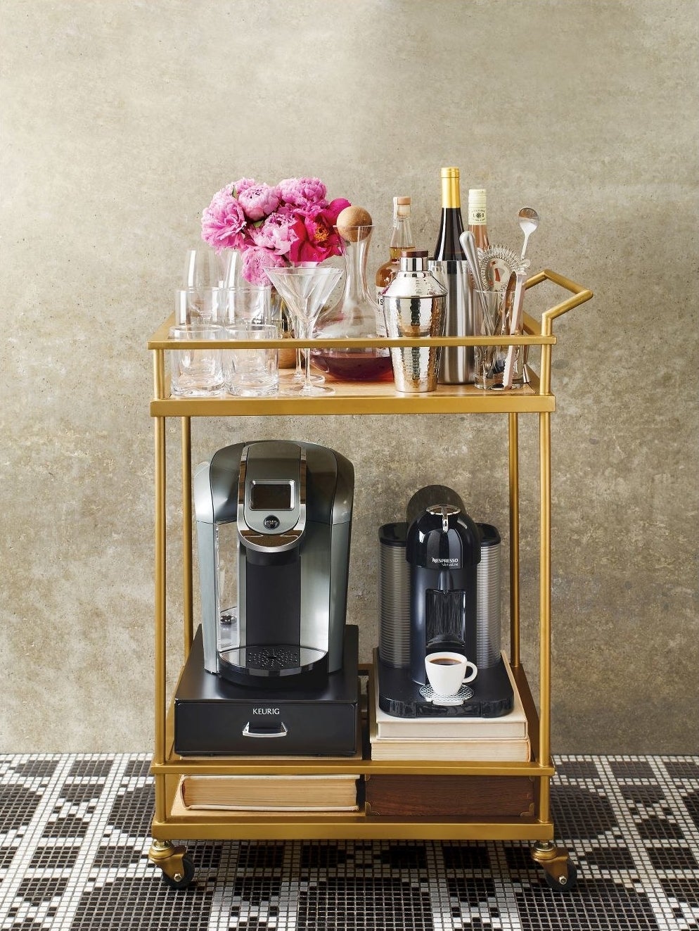 Wood and gold bar cart with black wheels carrying coffee machines on the bottom and cocktail shakers on top