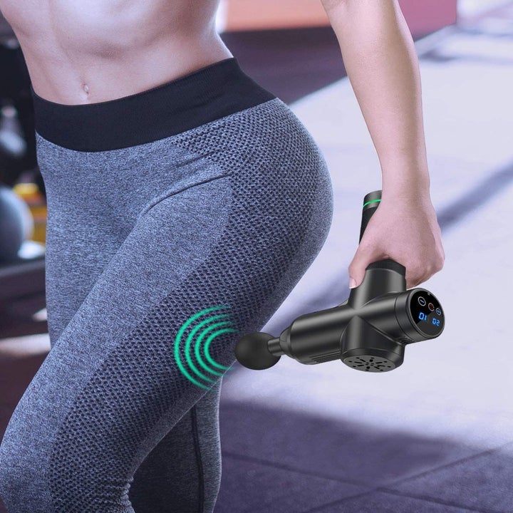 A person holding the massage gun up to their leg