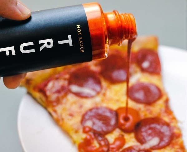 A person putting the truffle hot sauce on pepperoni pizza