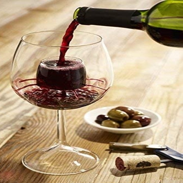 Stemmed wine glass with aerating piece in center, with wine being poured into center of glass and flowing out from the inner sides