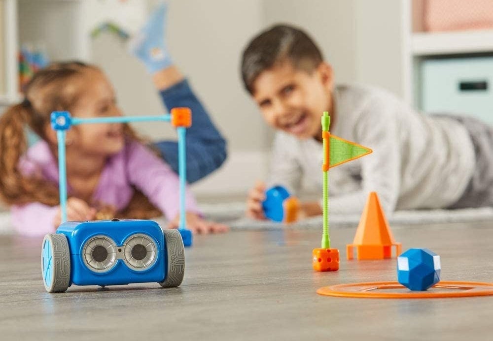 Two child models playing with wheeled blue robot