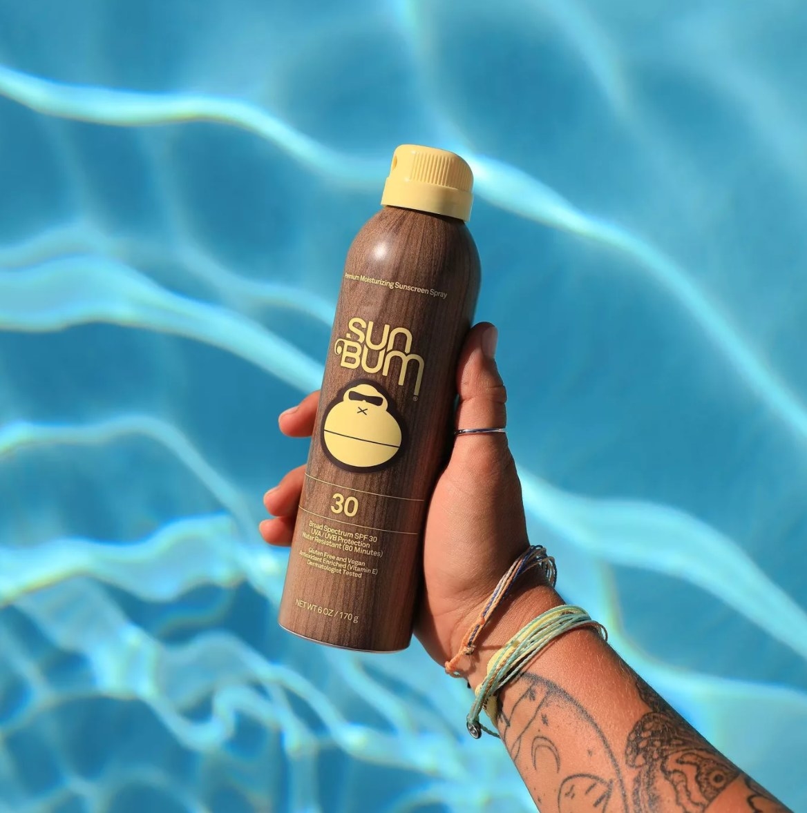 tattooed arm holding Sun Bum sunscreen over pool 
