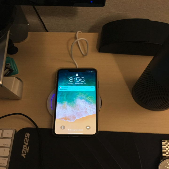 reviewer photo showing an iPhone charging on the white mirror charging pad on a nightstand 