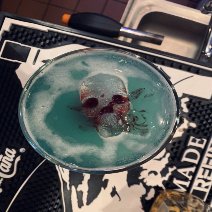 reviewer image of a skull ice cube partly submerged a blue frothy cocktail