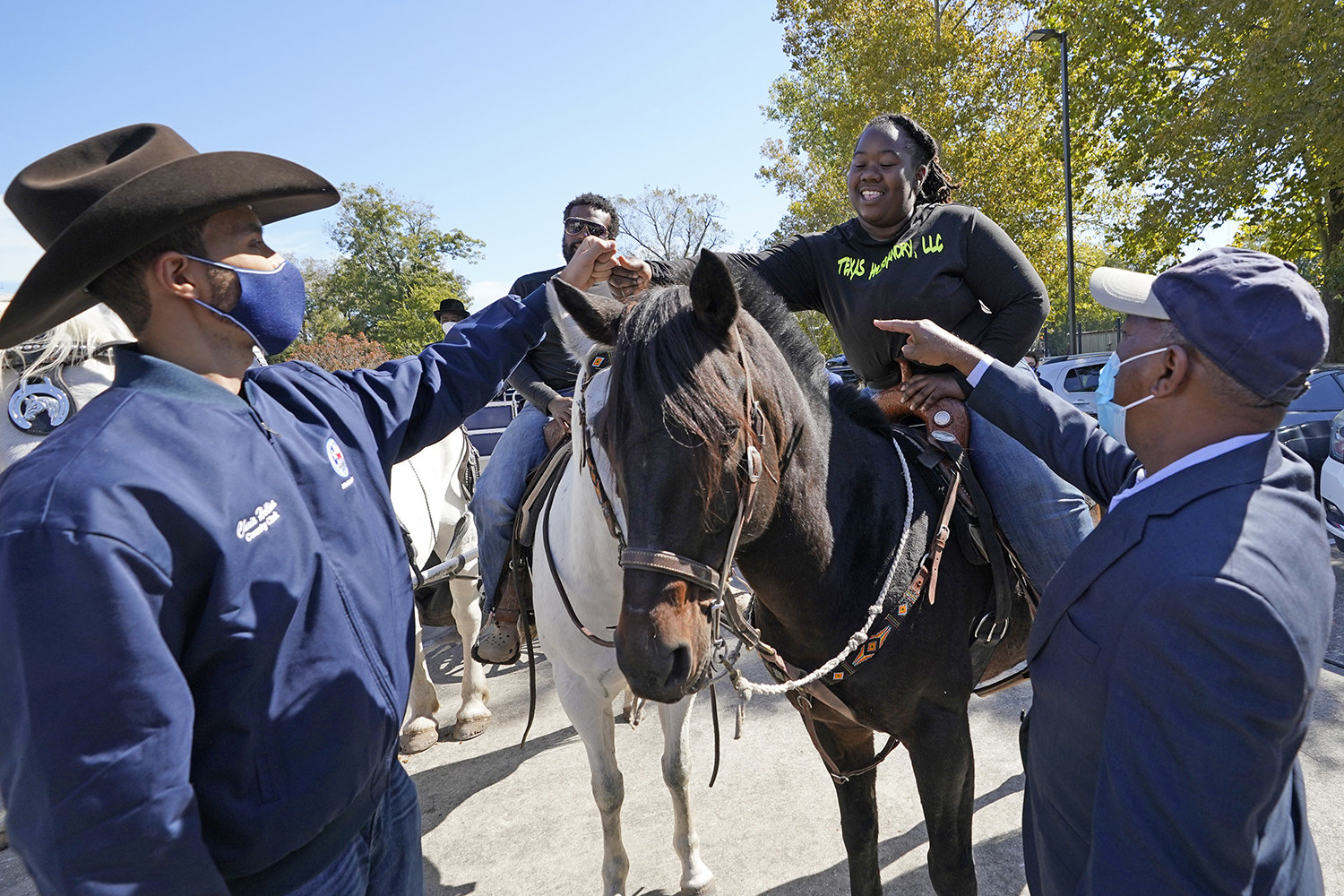 Two people on horseback fist bump with two men who are standing 