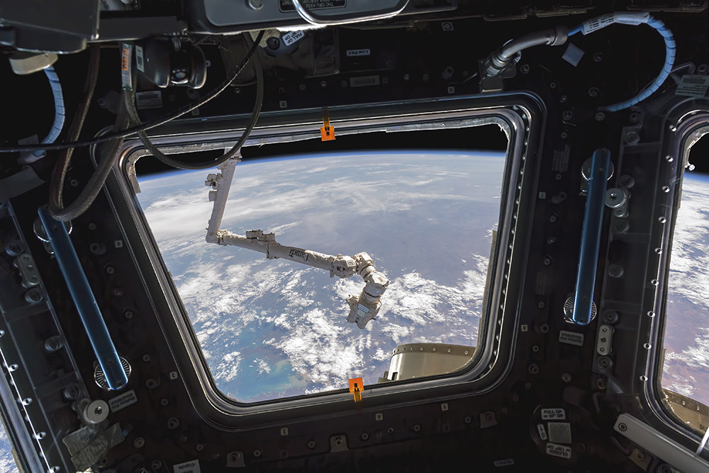 A robotic arm seen outside a window with Earth in the backgroud