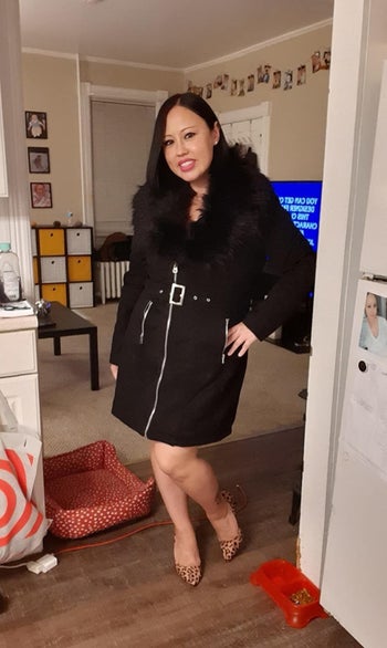 Reviewer wearing the knee-length jacket in black with silver long zipper and belt in the middle