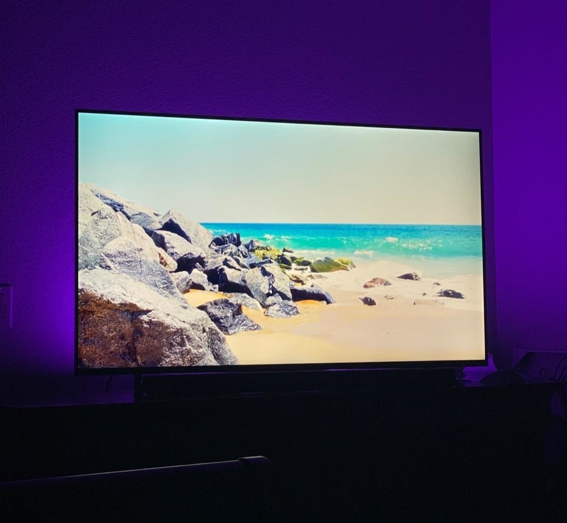 Reviewer pic of their tv with the lights behind it, with purple color all over the wall