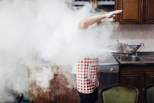 Young man standing in front of an oven with smoke filling the room.