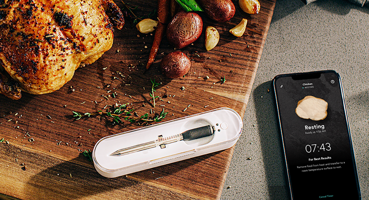 The Yummly Smart Thermometer and a smartphone next to a roasted chicken.