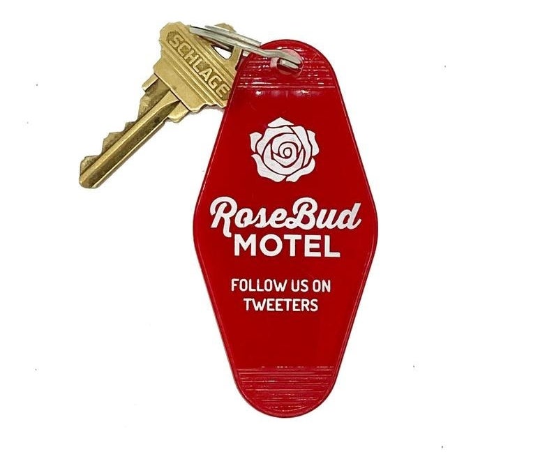 Red plastic keychain with white rose, name of motel, and &quot;follow us on tweeters&quot; printed on it