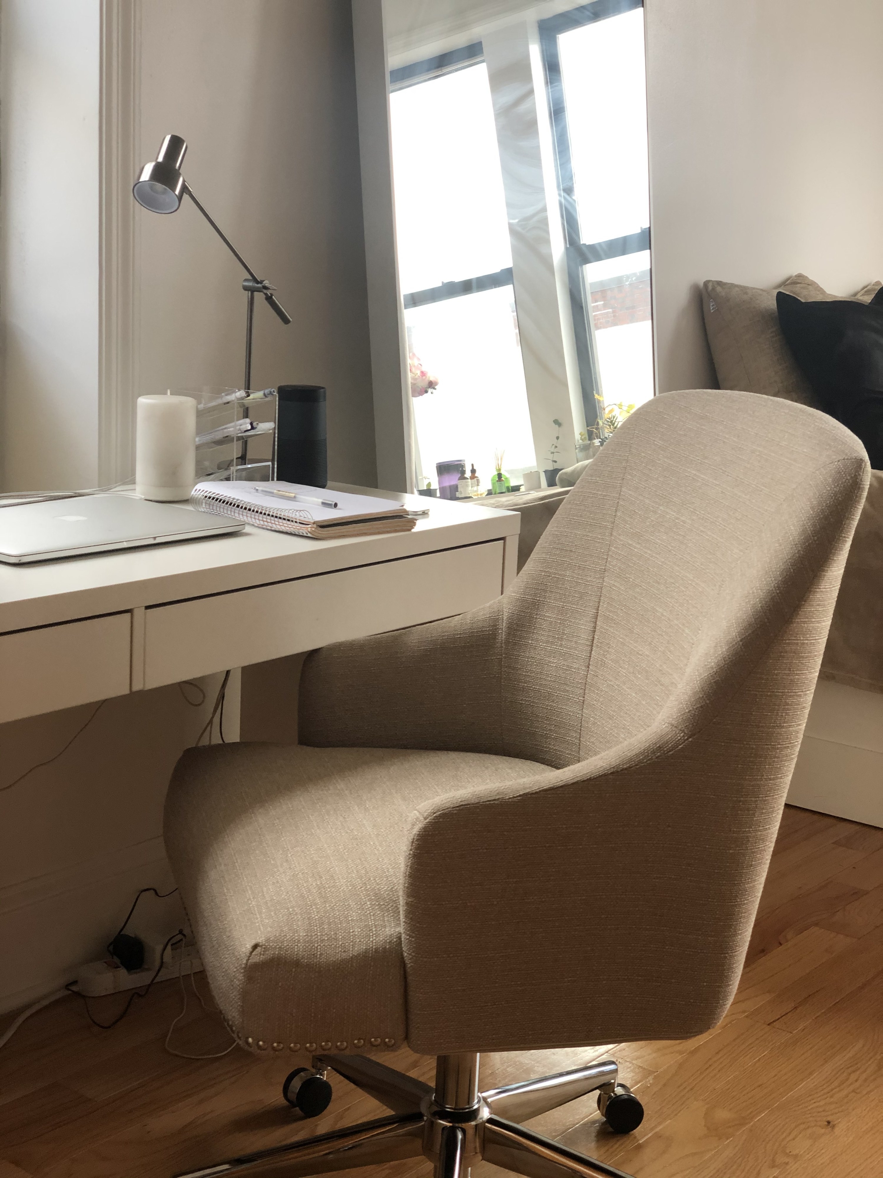 BuzzFeed writer&#x27;s chair in a brown-beige fabric with nailhead detailing around the bottom of the seat and metal rolling legs