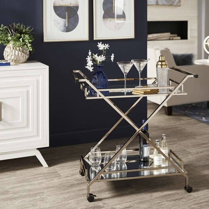 The two-layer rolling cart with mirrored shelves connected by criss-crossing light gold beams and handles