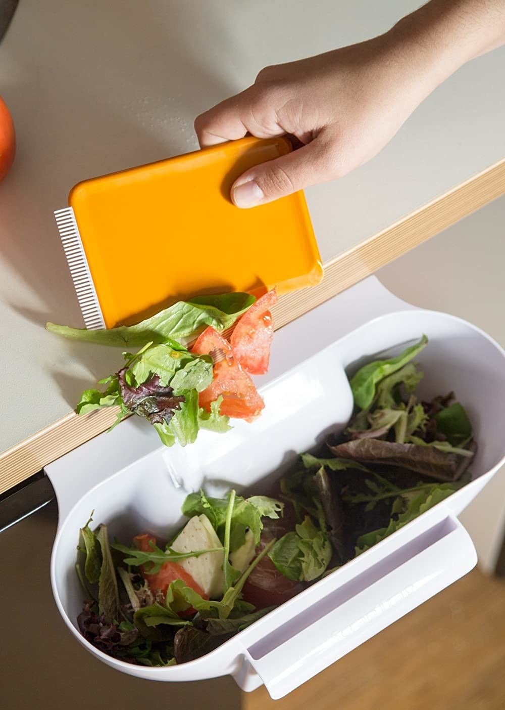 A person scoops kitchen scraps off the counter and into the cabinet-mounted trap