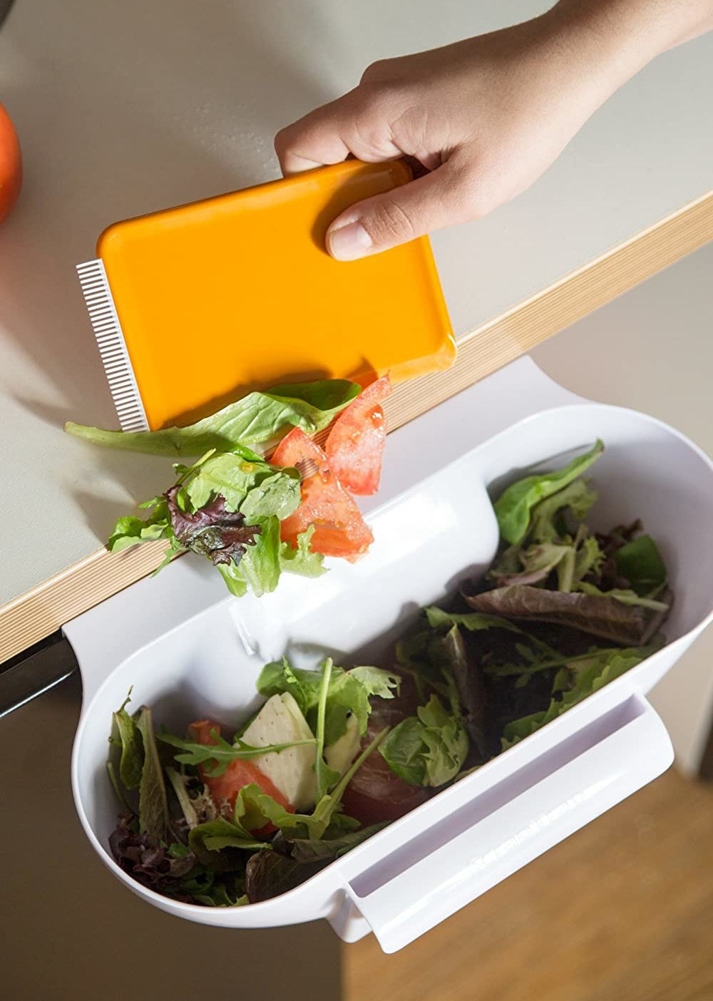 A person scoops kitchen scraps off the counter and into the cabinet-mounted trap